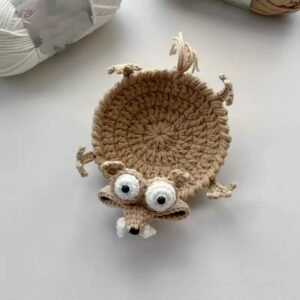 Handmade beige crochet animal coaster with big eyes and small teeth, viewed from the front.