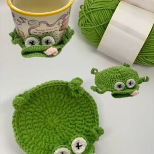 Bright green crochet frog coaster shown with a cup and yarn.